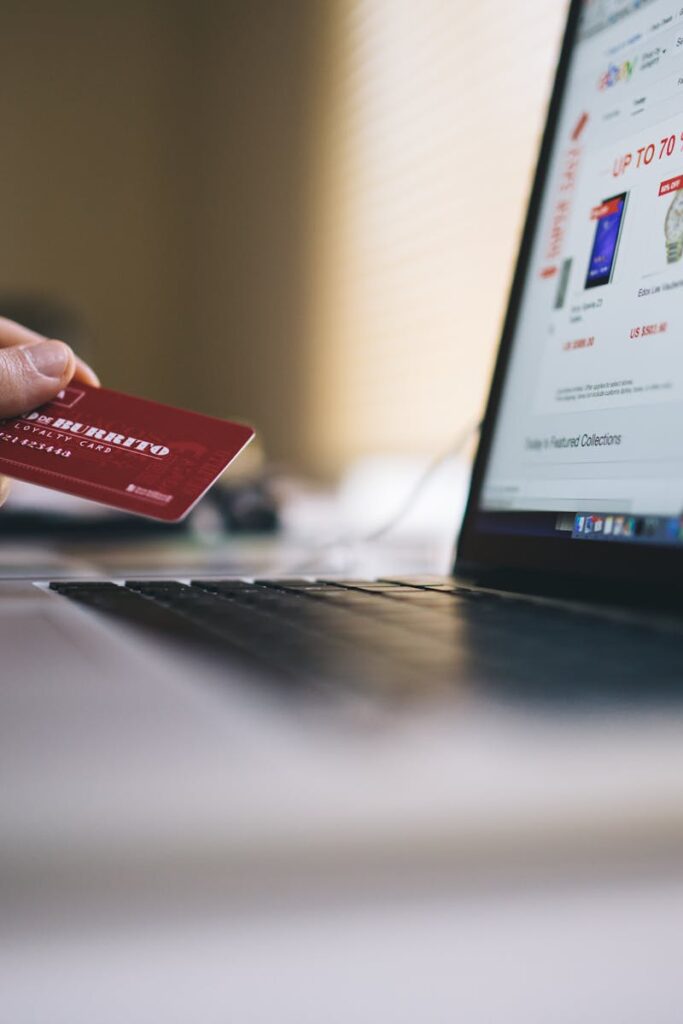 Person holding a credit card while shopping online on a laptop, indicating ecommerce transactions.